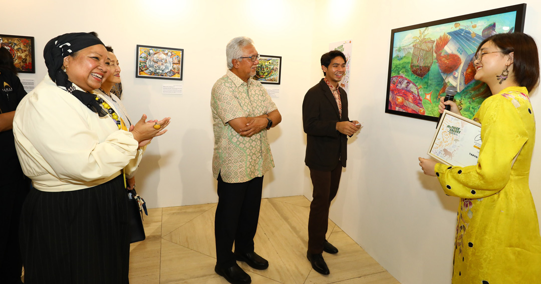 Tan Sri Dato' Sri Ir. Zamzamzairani Mohd Isa, Chairman of Maybank & Maybank Foundation (center, in bright batik) and Izlyn Ramli, Head Group Corporate Affairs Maybank & CEO of Maybank Foundation (in white) admiring the winning piece called ‘Think Out of The Room for Growth’ by Taryn Lung Sze Hui from the Malaysian Institute of Art (MIA), the First Prize winner in the University (Illustration) category. The artist explains that the artwork reflects Maybank’s TIGER values and the Sustainable Development Goals (SDGs) through the artist’s whimsical portrayal of nature’s beauty and significance.