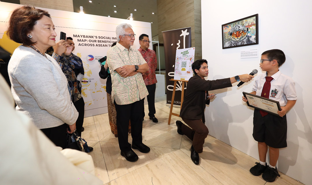 Teng Ziyu from Stonyhurst International School, Penang, the First Prize winner in the Primary School category, explains the inspiration behind his drawing “One Team, One Tiger” that highlights a mechanical armour for a tiger symbolising resilience and strength. Listening attentively to the young artist are Tan Sri Dato' Sri Ir. Zamzamzairani Mohd Isa, Chairman of Maybank & Maybank Foundation (in bright batik), Shahril Azuar Jimin, Group Chief Sustainability Officer (in red batik) and Fauziah Hisham, member of the Maybank Board of Directors (in light grey).